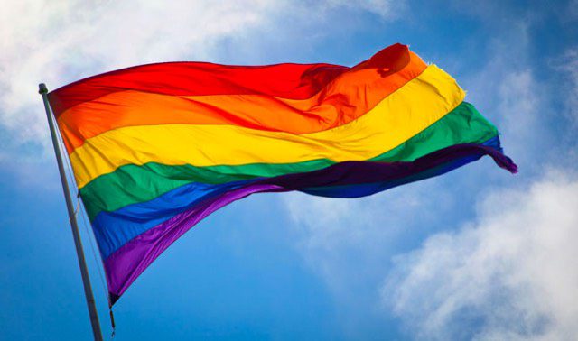 A rainbow flag flying on a blue sky