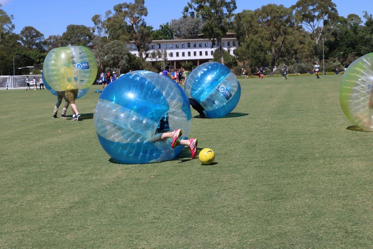 People playing bubble soccer on a field.