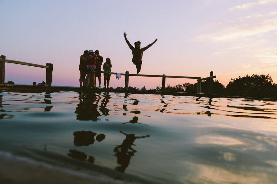 A young person jumping into an outdoor pool surrounded by friends.