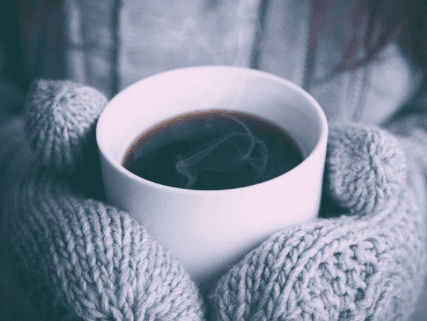 hands in mittens holding a steaming cup of black coffee
