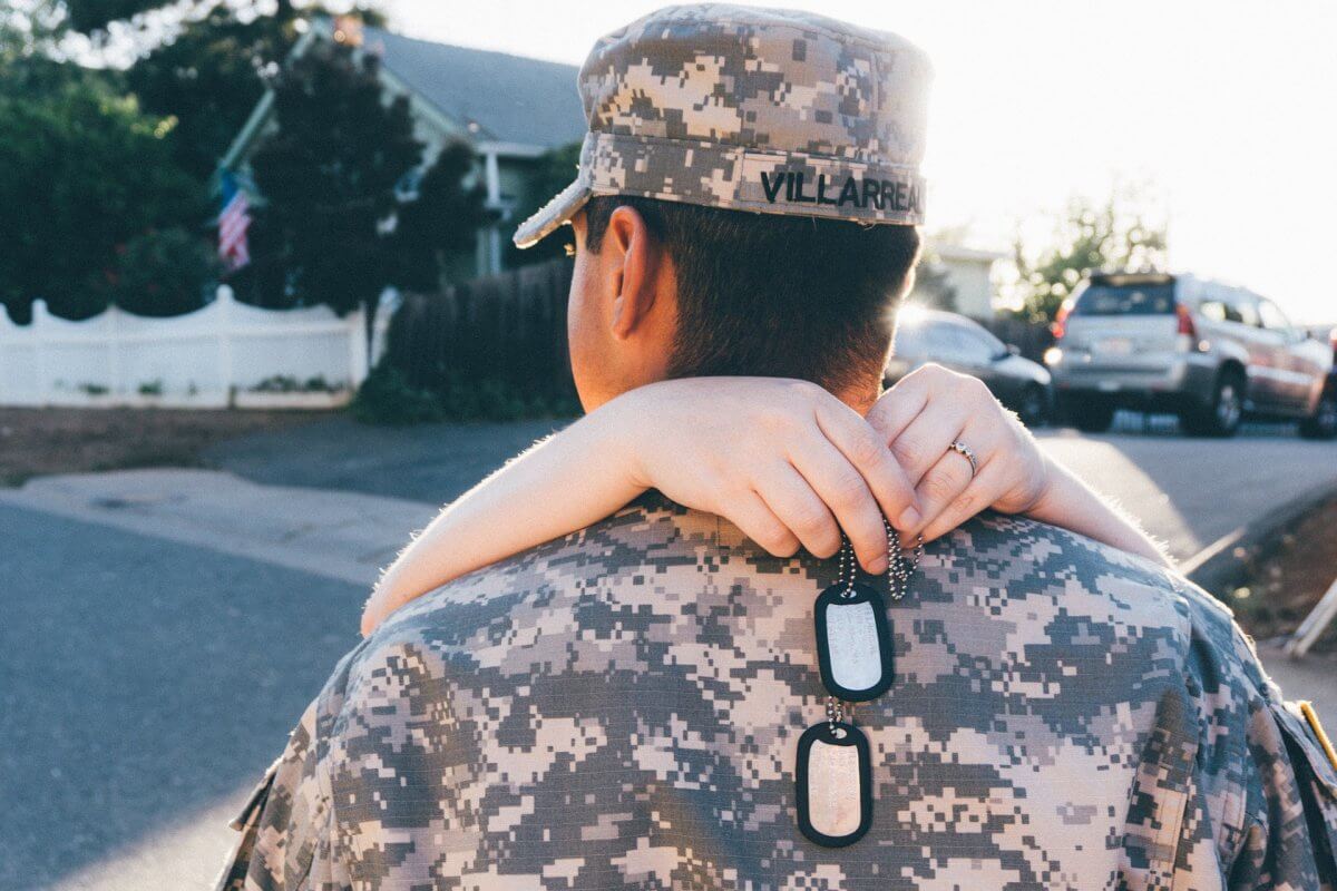 A military service person with their back facing the camera. They are being hugged.