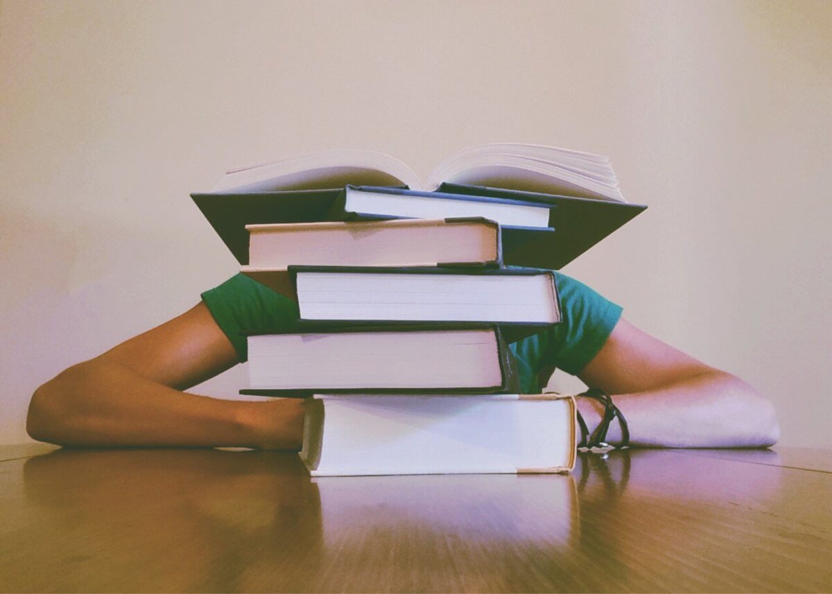 Student with their head on a desk behind a pile of books.