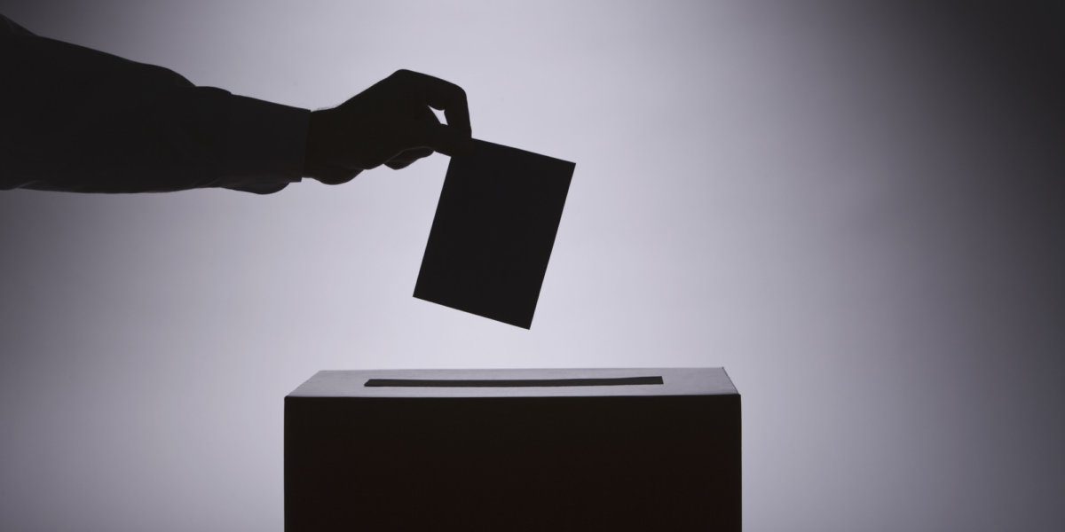 silhouette of a hand putting a ticket into a ballot box