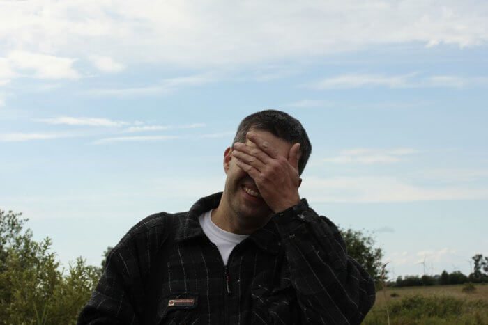 Embarrassed man shielding his eyes but smiling.