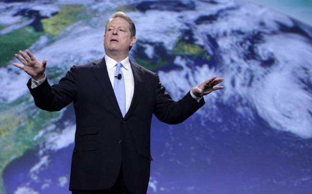 Al Gore, wearing a suit, is extending his arms dramatically in front of an image of the Earth.
