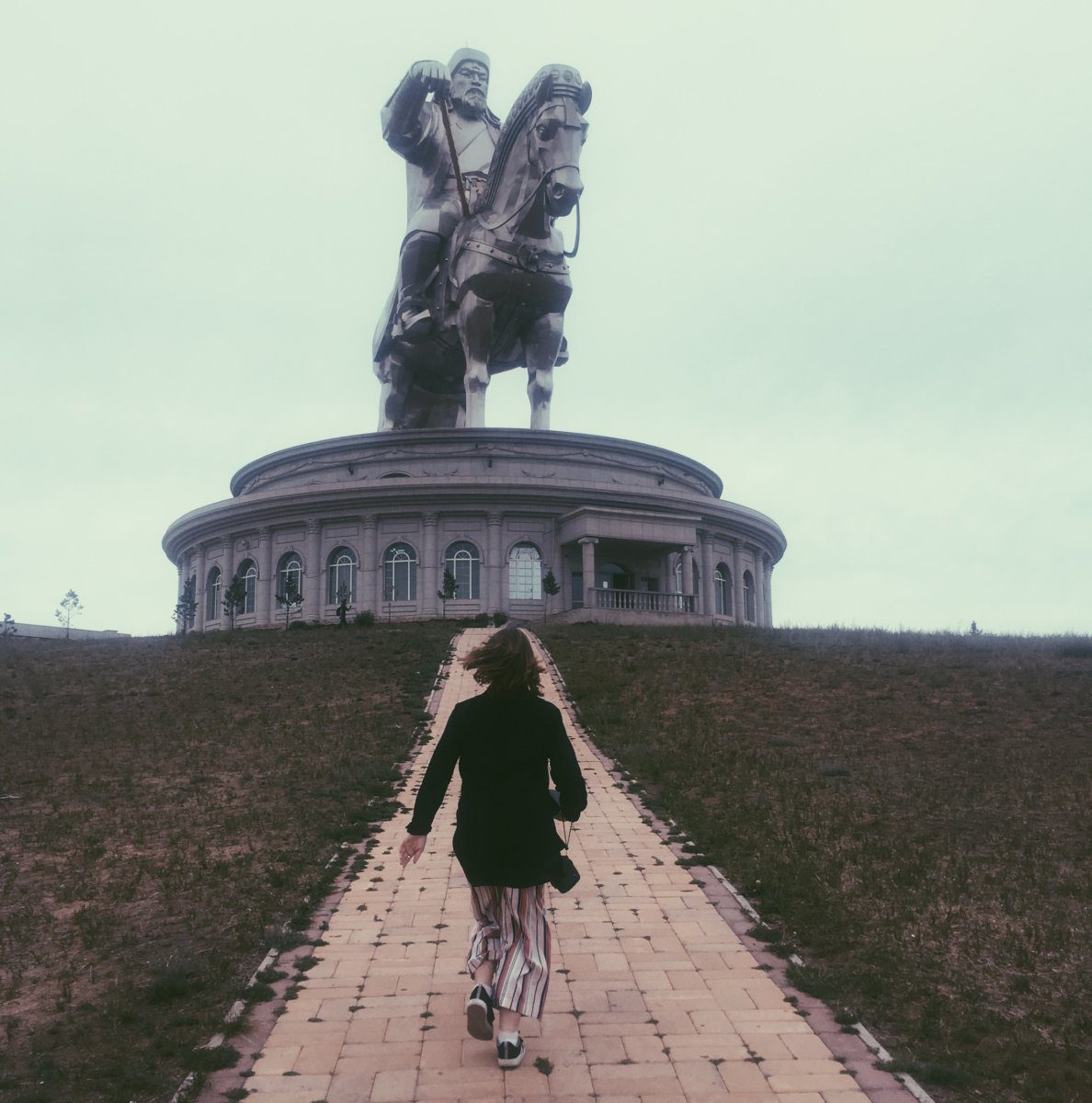 girl running towards a statute of a man on horseback in Mongolia