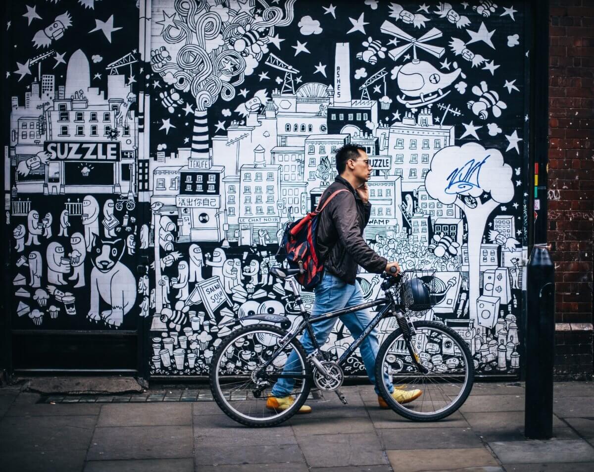 Man with bicycle walking past street art