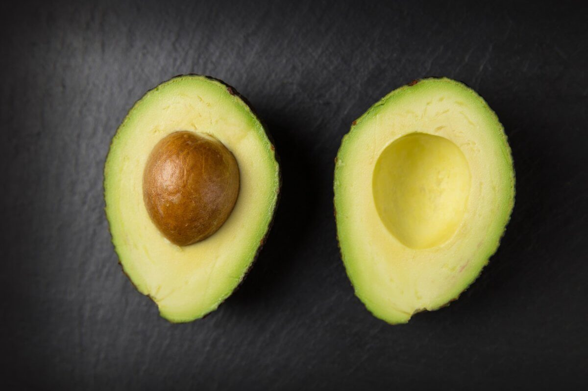 Avocado cut in half with inside facing up on a dark wood background.