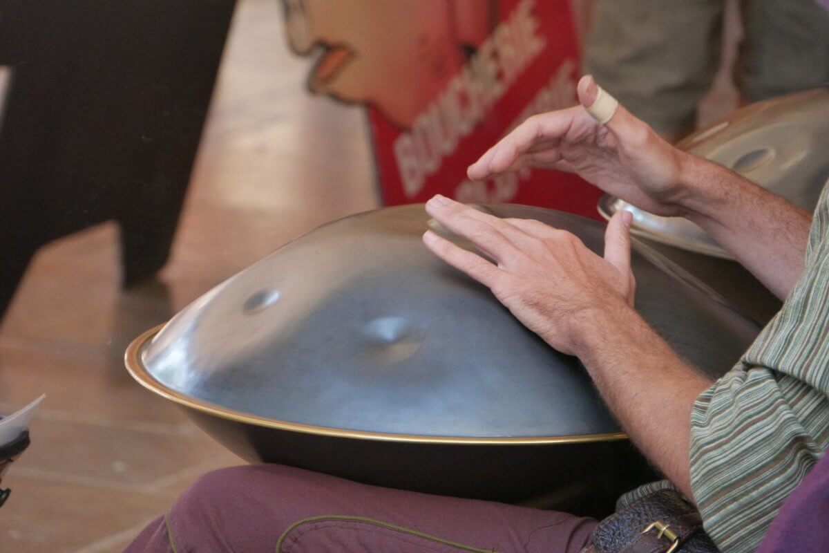 Hands playing metal drum in person's lap