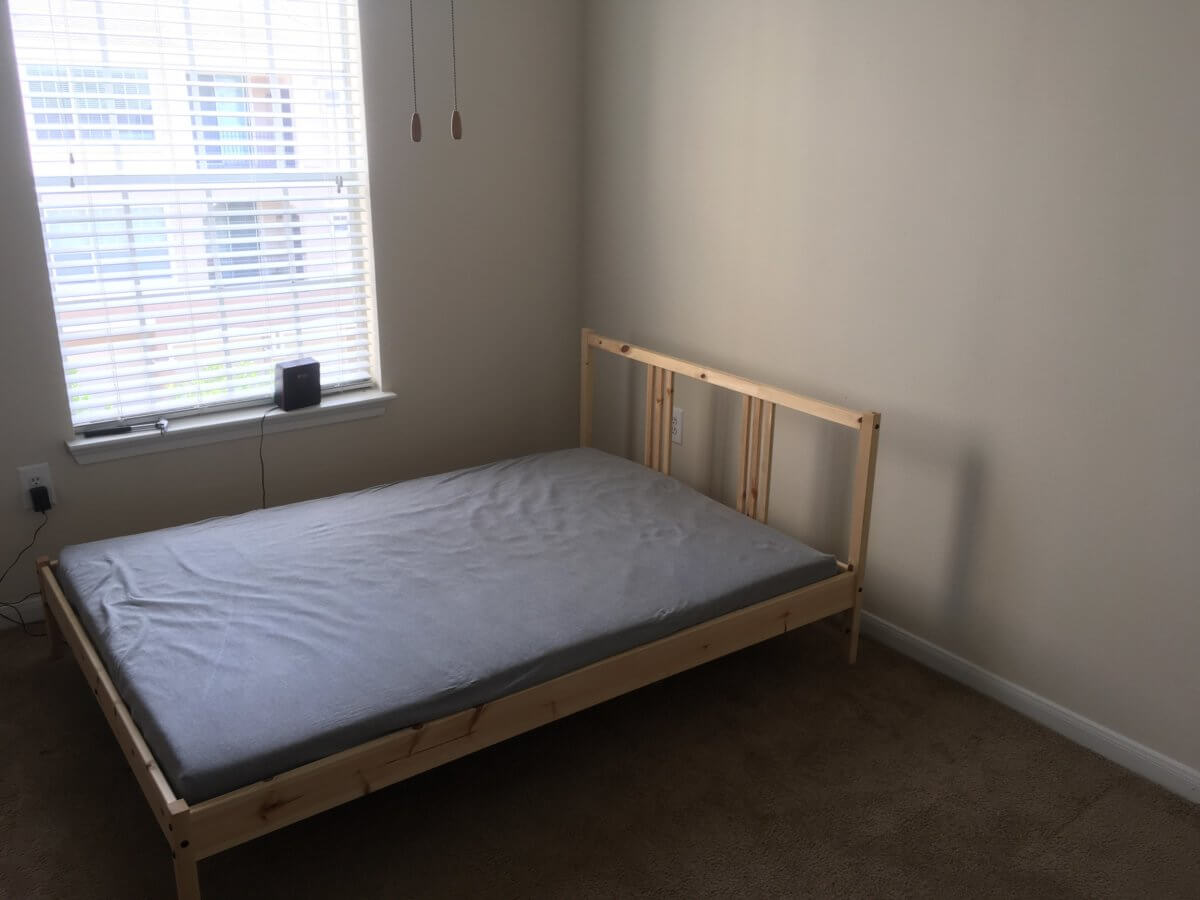 A single bedroom with a double bed mattress, covered with a grey sheet.