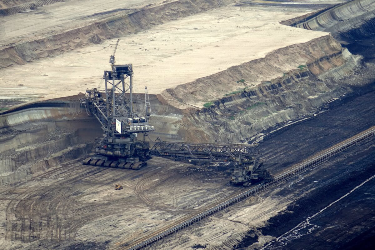 Image features a large surface mine, which looks like an area of flat rock-slab with some machinery in the centre