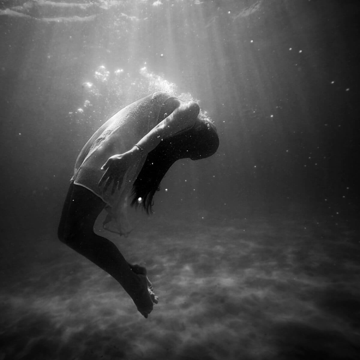 A woman underwater with light shining on her, struggling for air.