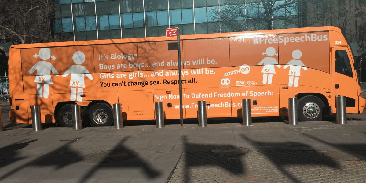 Orange bus with writing on the side, reading: "It's Biology. Boys are boys... and always will be. Girls are girls... and always will be. You can't change sex. Respect all. #FreeSpeechBus"