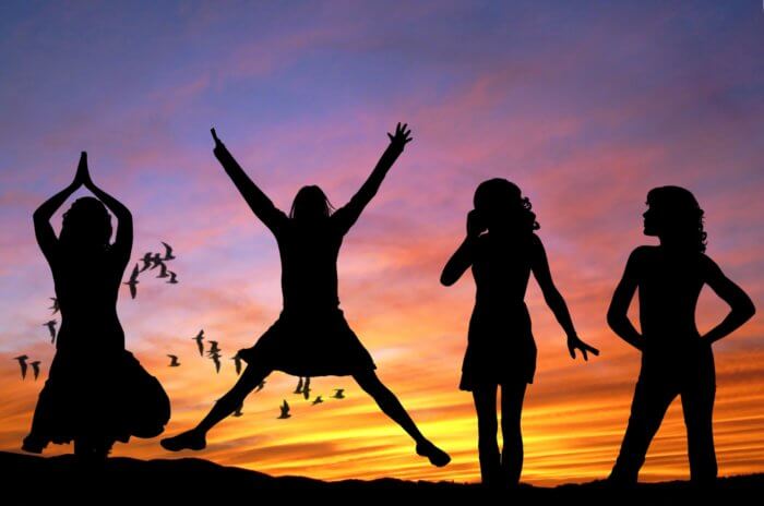 Image conatins the silhouettes of 4 women in a row standing in front of a sunset background. One is jumping in a star shape.