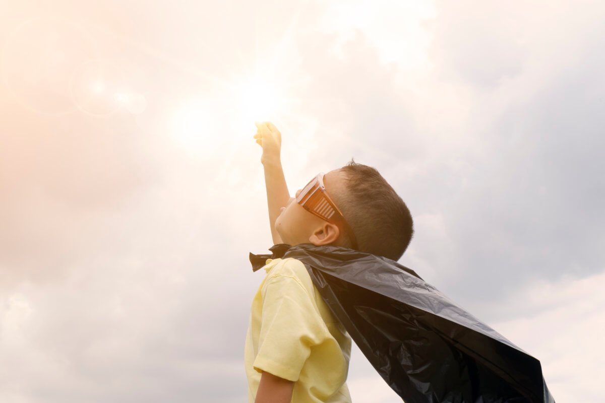 The image features a young child holding one closed fist towards the sky, whilst wearing a plastic bag cape