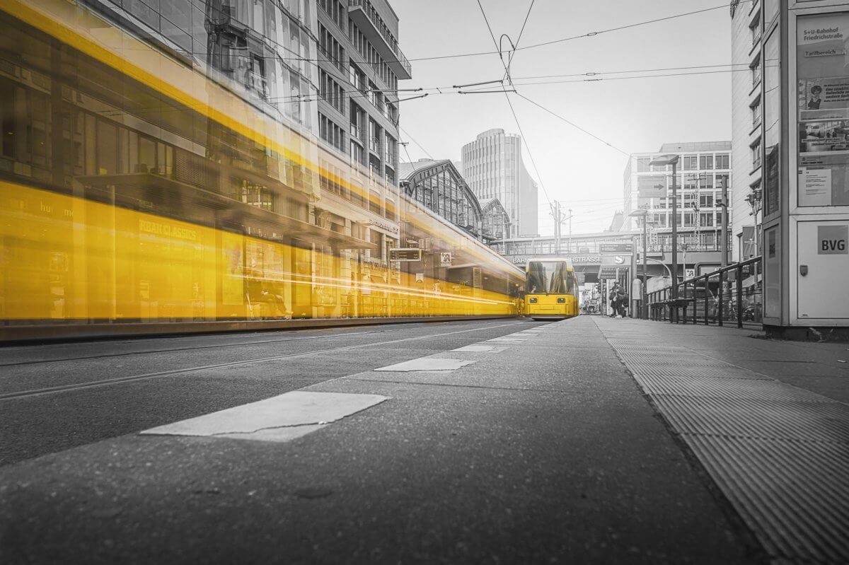 Yellow train travelling along a black and white street scene. The train is blurred because of the speed at which it is travelling.