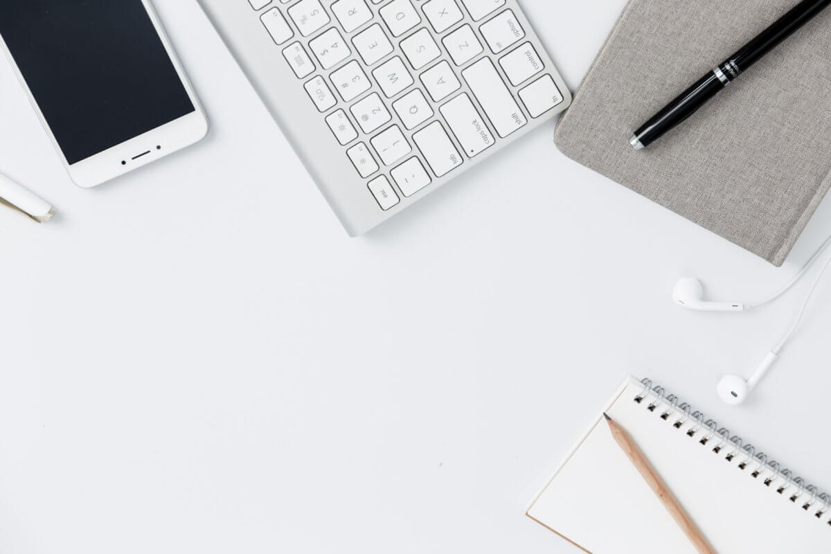 Top-down view of a white desk with stationery, phone and computer keyboard visible.