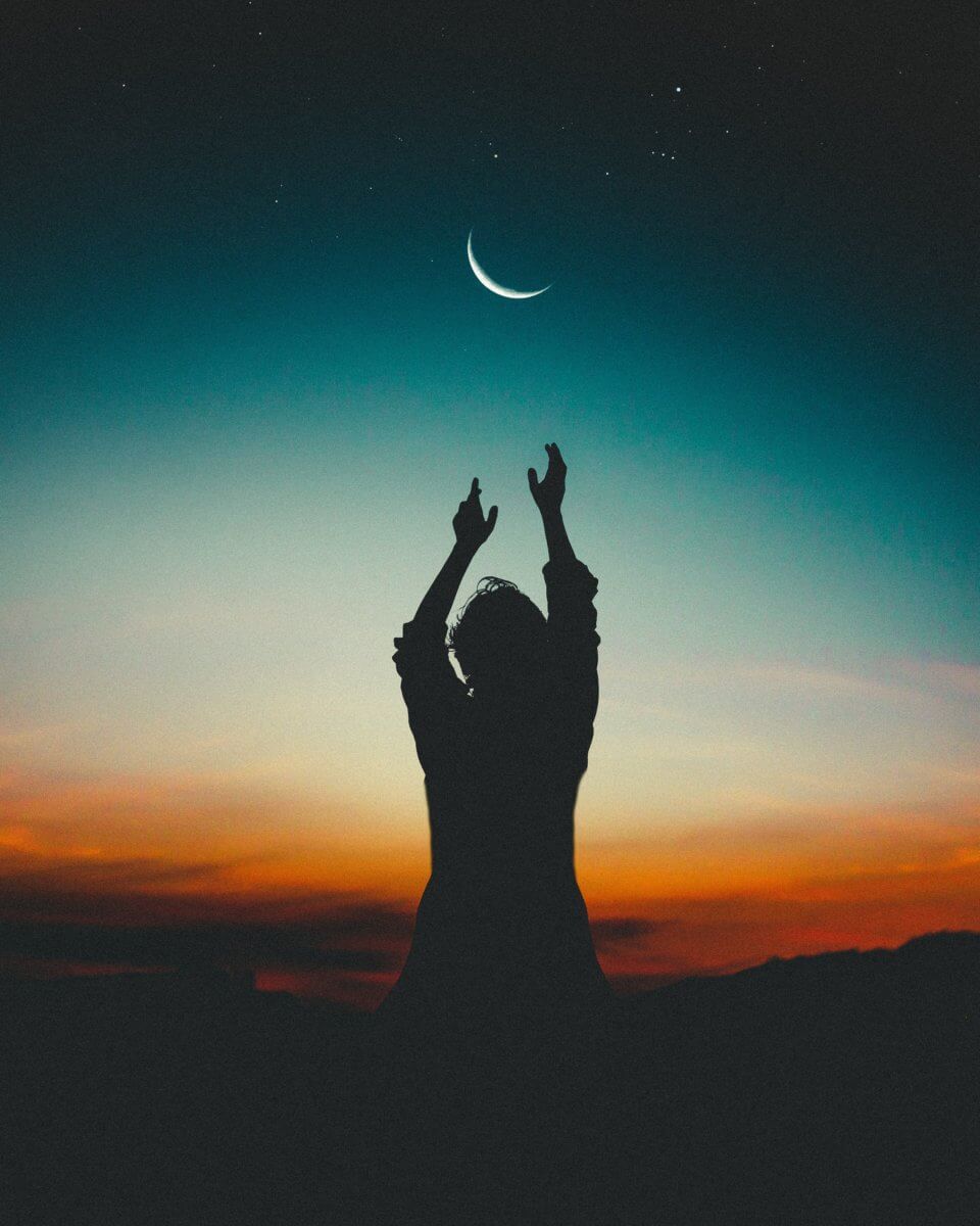 A silhouette of a person gesturing towards the moon.