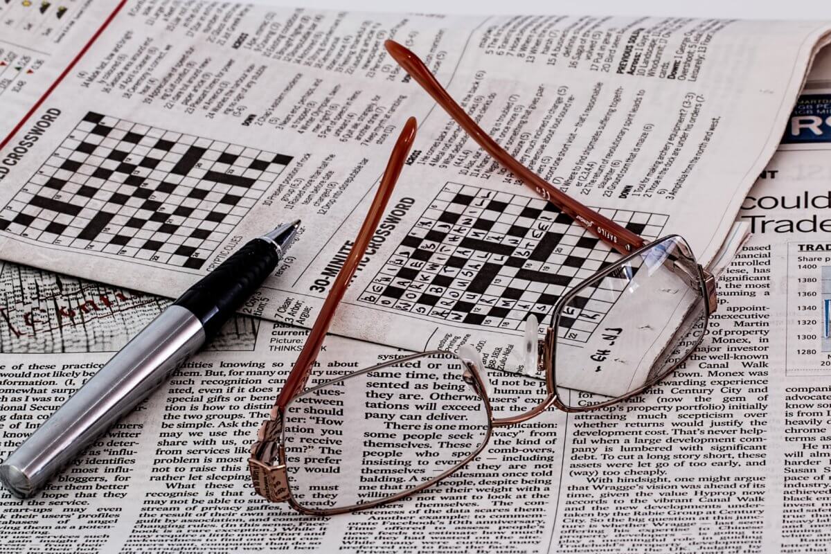 Crosswords with glass and a pen laying on them.