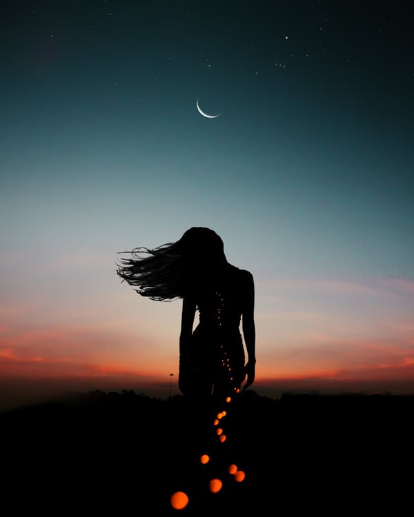 Female silhouette with setting sky and crescent moon in the background