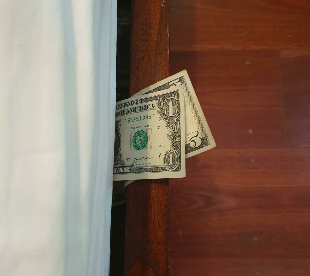 A photograph by Maddy Watson of cash money sticking out from under a mattress