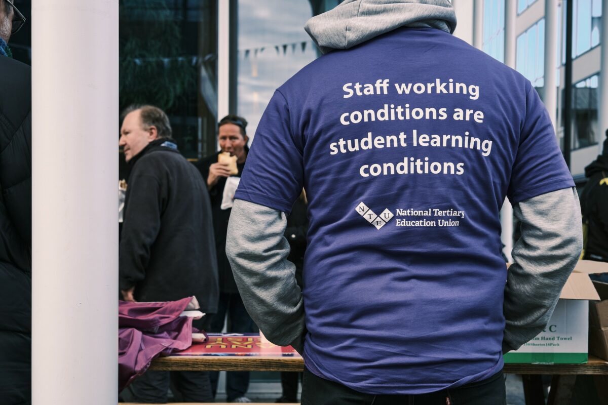 A person wearing a t-shirt with the slogan "Staff working conditions are student learning conditions"